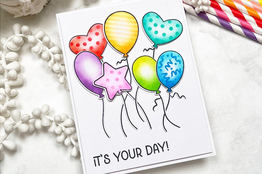 A handmade card featuring 7 stamped , ink blended and stenciled floating, dancing balloons.