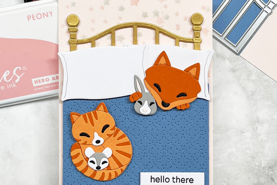 Handmade card featuring a die cut fox and orange tabby cat in  a brass bed  with a blue quilt.